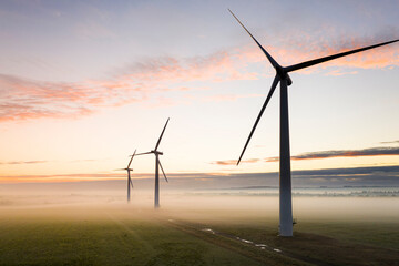 Aerial view of three wind turbines in the early morning fog at sunrise in the English countryside