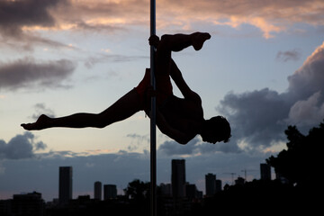 Muscular male pole dancer, holding a pose on a pole set outdoors. Silhouette shot with Tel Aviv...