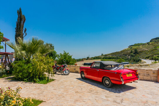 Omodos, Cyprus - June 7, 2018: Colorful scene of a resort island in the Troodos Mountains. Beautiful red car and a red motorcycle on the paved area at the winery.