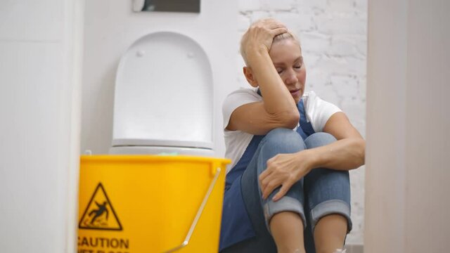 Tired woman sitting on bathroom floor with cleaning supplies and equipment.