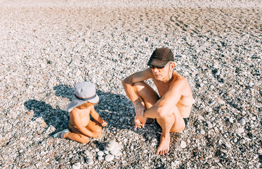 Toddler girl and grandfather playing with pebbles on beach