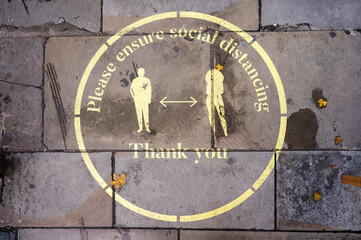 An overhead shot of a yellow Covid 19 social distancing sign painted on the sidewalk in Covent Garden