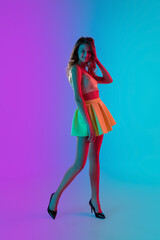 Dancing. Beautiful seductive girl in fashionable yellow skirt on gradient pink-blue neon background. Full-length portrait. Copyspace for ad. Flyer design. Summer, fashion, emotions concept.