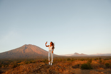 Young woman making selfie on her phone on background of Agung volcano during the trip on Bali island