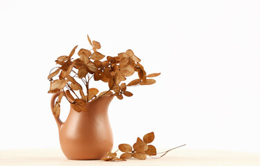 Dry brown hydrangea flowers in a clay jag on a wooden table