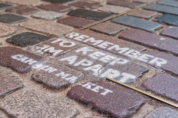 A shallow focus view of a painted sign on a cobbled floor reminding people to social distance at Camden Market due to the COVID-19 pandemic