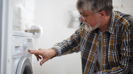 Side view of senior man turning on washing machine in bathroom