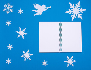 Obraz na płótnie Canvas Christmas and new year flat composition with white blank notepad, white angel playing trumpet and snowflakes
