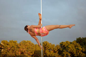 Young Middle Eastern pole dancer, holding a pose on a pole set in an urban park.