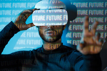Young man in futuristic costume on blue neon light digital interface background. Guy using VR helmet. Augmented reality, virtual reality, future technology, game concept.