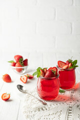 Sweet dessert jelly pudding with strawberries in glass jar on white background