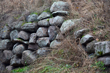 Retaining wall made of natural stone in dry brown grass in the landscaping of an old neglected park