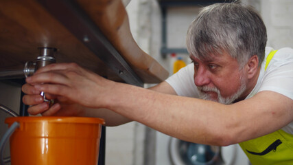 Male plumber working to fix leaking sink in home bathroom