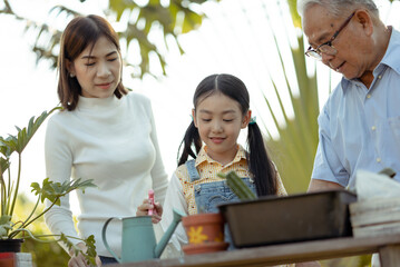 Asian grandpa with child girl planting young tree in the black soil	
