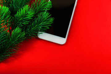 Winter christmas composition, white phone and fir branches, red background, copy space, flat lay, banner