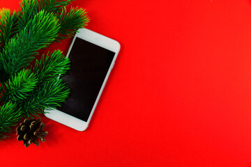 Winter christmas composition, phone, fir branches and cones, red background, copy space, flat lay, banner
