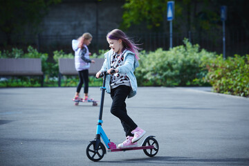 Active girls riding kick scooter and skateboard in skate park. Children having free time playing. The concept of a healthy lifestyle. Kids sport. © sarymsakov.com