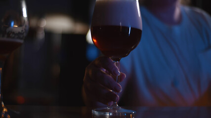 Bartender puts glass of light beer with foam on wooden table in pub