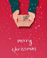 Female's hands in pullover holding Christmas gift box decorated with evergreen branch on red background with snow. Christmas and New Year banner.