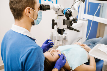 Naklejka na ściany i meble A dentist looking to the microscope at the patient's teeth