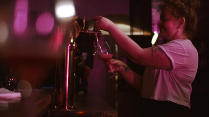 Side view of woman bartender pouring beer from tap in glass at pub