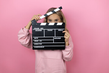 Young beautiful child girl standing over isolated pink background holding clapperboard very happy