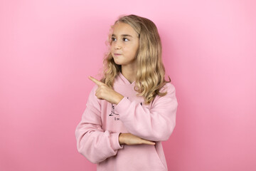 Young beautiful child girl standing over isolated pink background smiling happy pointing with hand and finger to the side