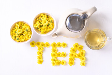 Organic Chrysanthemum flower tea in a cup and teapot with TEA alphabet made from Chrysanthemum flower on white background, Healthy Herbal drink, Top view