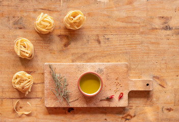 Fototapeta na wymiar Oil, chili and rosemary on a wooden cutter on a table with four tagliatelle pasta nests