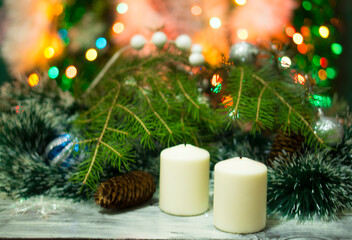 Christmas background with fir tree, balls, garlands. Beautiful festive background with tinsel. Blurred background with lights from Christmas lights. Candles in the foreground without fire, smoke 