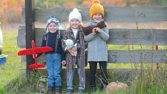 Happy family children kid together on an autumn field in the countryside. Group of joyful children with toys stand amicably on the background of wooden care. Happy laughing children.