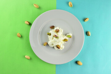 Pistachios on fresh cheese, served on a white porcelain plate. Two-color background 