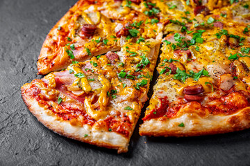 Pizza with Mozzarella cheese, backon, ham, tomato sauce, pepper, sausage, pickled cucumbers and onion. Italian pizza on Dark grey black slate background