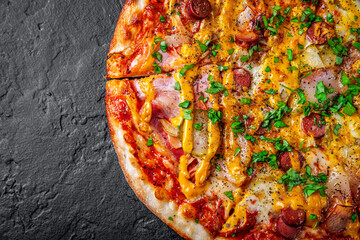 Pizza with Mozzarella cheese, backon, ham, tomato sauce, pepper, sausage, pickled cucumbers and onion. Italian pizza on Dark grey black slate background