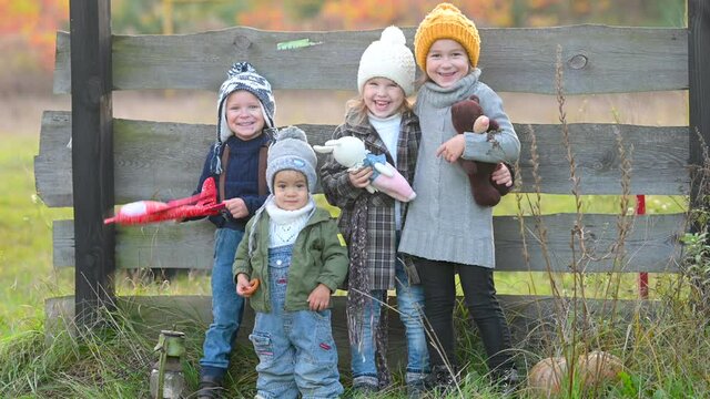 Happy family children kid together on an autumn field in the countryside. Group of joyful children with toys stand amicably on the background of wooden care. Happy laughing children.
