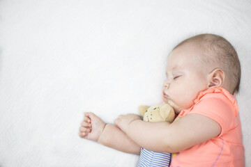 Newborn baby girl sleeping sweetly on a white bed with a toy in an embrace
