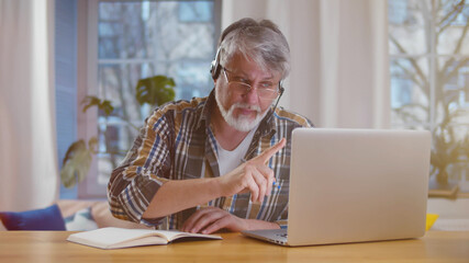 Aged man with headset and laptop computer having video conference at home office