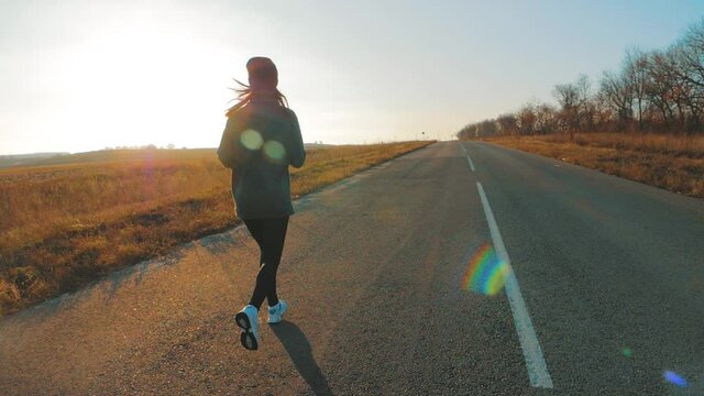 Young fitness sport woman running on road at sunset. Athlete runner feet running on road, slow motion.