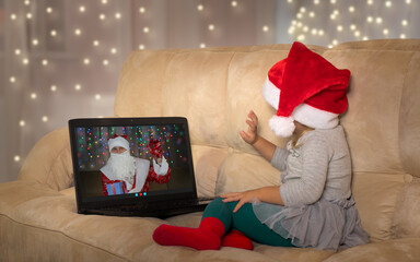 Kid in santa hat is having web chat call with Santa. Little girl listening Santa Claus online.