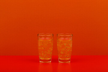 Fototapeta na wymiar Two orange drinks in shot glasses on red background