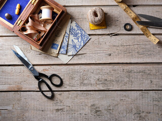 Sewing and Embroidery work table flat lay with sewing box, fabric scissors, thread, vintage design sheets, thimbles, needles and ribbon arranged with copy space