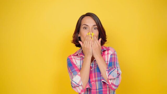 Sending a french air kiss beautiful girl dressed in a plaid shirt and dark hair on a yellow background. Human emotions, facial expression concept. High quality 4k footage. 