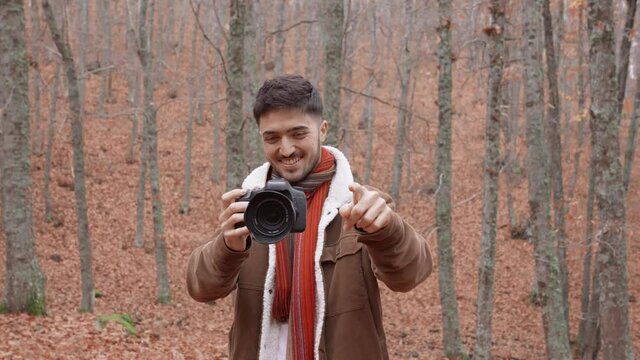 Medium shot Caucasian boy in forest with red and orange autumn leaves photographing with a professional camera