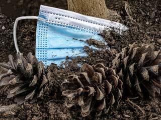 Dirty blue medical mask buried in the ground by a tree