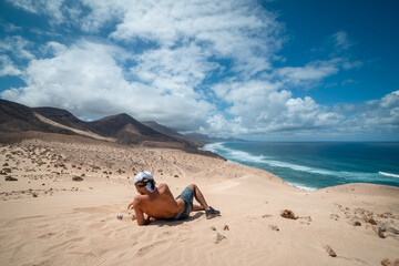 Fototapeta na wymiar young man take a rest to watches the landscape. Jandía dunes . Fuerteventura. Canary Islands