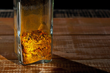 A mixture of various spices in a glass jar close up. Spices on an old shabby board. Free space and copy space for text near condiments. Contrasting dramatic light as an artistic effect.