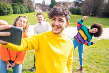 Four people multiethnic friends having fun outdoor using smartphone taking selfie