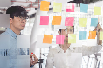 Business manager showing idea for her team and stick many memo paper on glass window to success working in business meeting  creative office, planning and management concept.