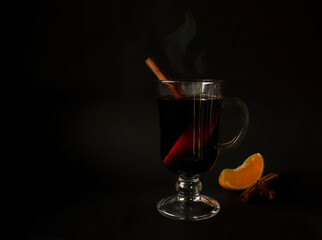 Hot mulled wine with steam, slice of orange, star anise and cinnamon stick on black background. Low key photography. Space for text. Christmas winter drink