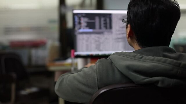 Selective focus to the back of the programmer is sitting to develop the program with blurry data coding in monitor. Developing programming and coding technologies in a software develop company office.